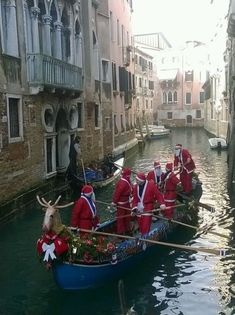 some people in red and white outfits are riding on a boat down a canal with reindeer heads