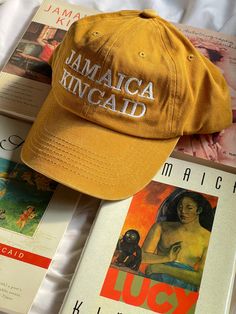 Jamaica Kincaid Womb House Books Hat. Adjustable cotton hat. Mustard yellow color. JAMAICA KINCAID on front, Womb House Books on back. Hat orders are sent every Monday and generally take two weeks to arrive. Yellow Cap For Vacation, Yellow Vacation Cap, Yellow Cotton Dad Hat, Yellow Cotton Curved Brim Dad Hat, Yellow Cotton Dad Hat With Curved Brim, Yellow Cotton Dad Hat, One Size Fits Most, Yellow Cotton Hat (one Size Fits Most), Adjustable Yellow Cotton Hat, Yellow Wide Brim Cotton Hat