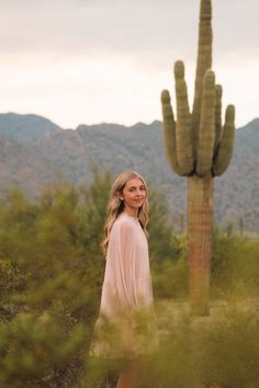 a woman standing in front of a tall cactus