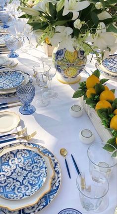 a table set with blue and white plates, lemons and flowers in vases