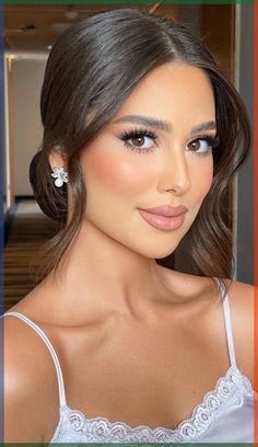 a woman with brown hair wearing a white bra top and earrings, looking at the camera