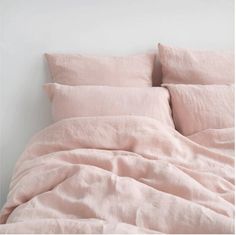 an unmade bed with pink linens in a white walled room next to a wall