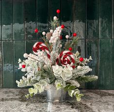 a christmas arrangement with candy canes and flowers in a silver bucket on a marble countertop