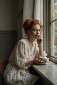 a woman sitting at a window sill holding a cup