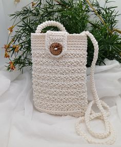 a crocheted white purse with a button on the front and strap around it