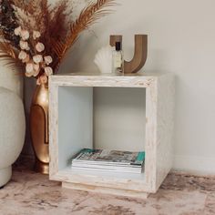 a white cube shelf with magazines and vases on it next to a wall mounted plant