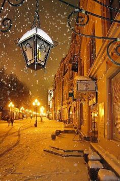 a street light hanging from the side of a building on a snow covered sidewalk at night