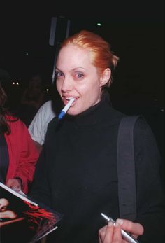 a woman with a toothbrush in her mouth is holding a notebook and smiling at the camera