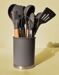 a cup filled with utensils on top of a table next to a yellow wall