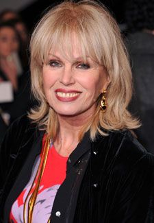 a woman with blonde hair smiling and wearing a red shirt, black jacket and gold earrings