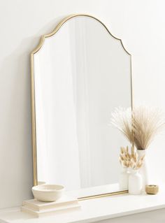 a mirror sitting on top of a white mantle next to a vase with dry grass in it