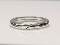 a white gold wedding ring with a twist design on the side, sitting on a table