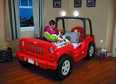 a man and boy are reading in a red jeep bed with lights on the headboard