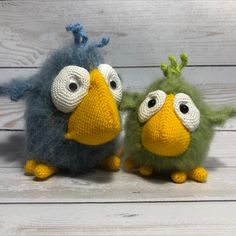 two knitted birds sitting next to each other on a white wooden surface with wood planks