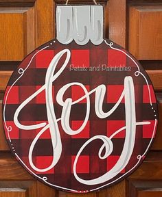 a red and black christmas ornament hanging on a door with the word joy painted on it