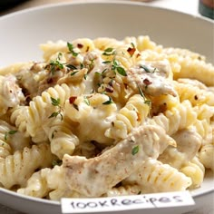 a white bowl filled with pasta covered in sauce and chicken meat on top of it