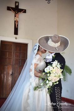 a bride and groom kissing in front of a cross