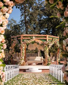 an outdoor ceremony setup with white chairs and flowers on the aisle, surrounded by greenery