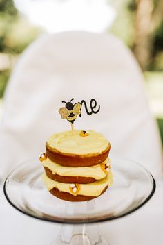 a cake on a glass plate with a small one topper in the shape of a bee