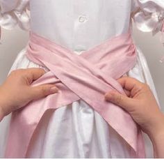 two hands are holding the back of a dress with pink ribbon on it and one hand is