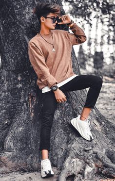 a young man sitting on top of a tree next to a tree trunk wearing white sneakers