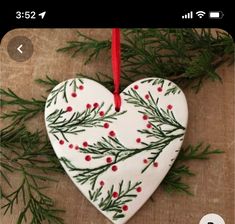 a heart shaped ornament hanging from a tree branch with red berries on it