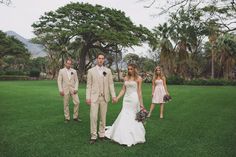 the bride and groom are holding hands while walking through the grass with their bridal party