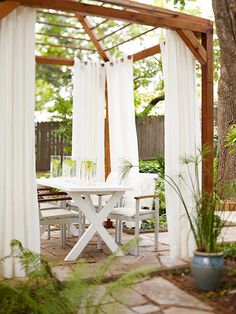 a white table and chairs under a pergolated arbor with curtains on the side