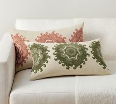 two pillows sitting on top of a white couch next to a pillow with green and red designs