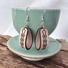 a pair of earrings sitting on top of a wooden table next to a green cup