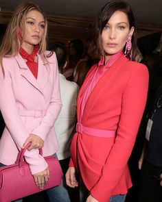 two women standing next to each other in front of a group of people wearing pink outfits