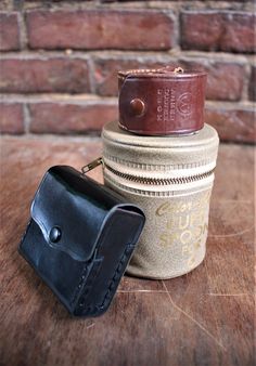 two leather wallets sitting next to each other on top of a wooden table in front of a brick wall