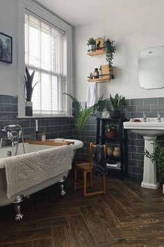 a bath tub sitting under a window next to a white sink and wooden flooring