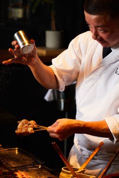 a chef is sprinkling sauce on food in a pot with chopsticks