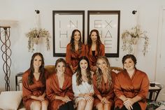 a group of women sitting on top of a couch in matching robes and smiling at the camera