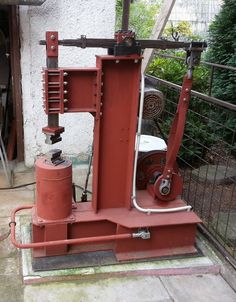 an old red machine sitting on top of a cement floor next to a fenced in area