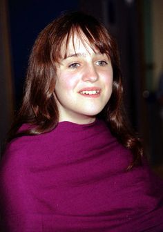 a woman in a purple shirt smiles for the camera while wrapped in a pink blanket