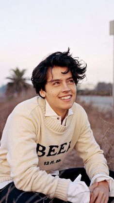 a young man sitting on the ground smiling