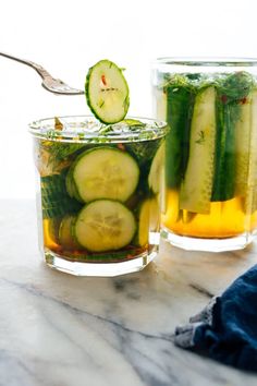 two glasses filled with cucumber and lemonade on top of a marble table