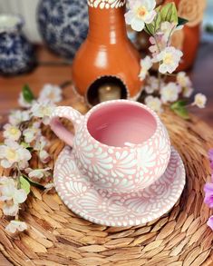 a pink tea cup and saucer sitting on a wicker tray with flowers in the background