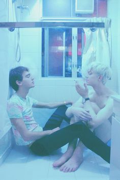 two people sitting on the floor in a bathroom next to each other with their hands together