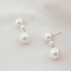 two white pearls are hanging from silver earwires on a white surface, with one pearl in the middle