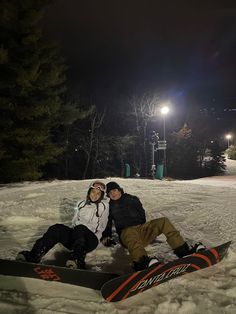 two snowboarders pose for a photo in the snow at night with their lights on