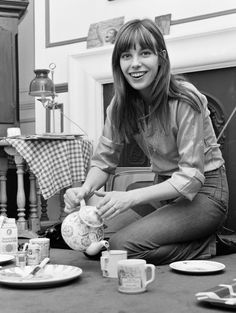 a black and white photo of a woman sitting on the floor with coffee cups, teapots and plates