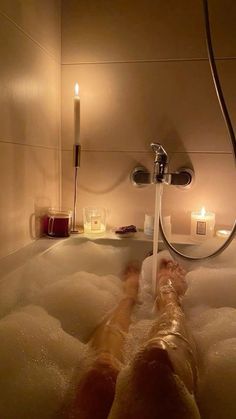 a person laying down in a bathtub with candles on the wall and soapy water