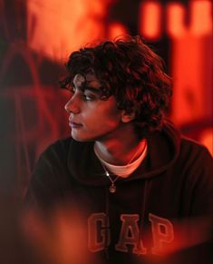 a young man with curly hair wearing a hoodie and looking off into the distance