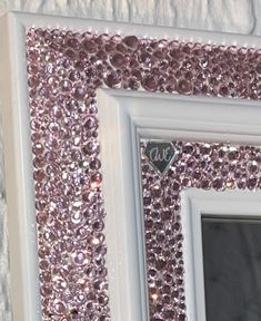 a white frame with pink and silver sequins on the wall next to a window