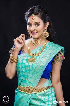 a woman in a green and blue sari with gold jewelry on her neck, posing for the camera