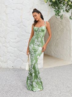 a woman in a green and white dress is standing by a wall with flowers on it