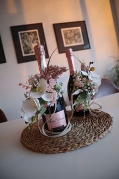 two wine bottles with flowers in them sitting on a wicker basket next to each other